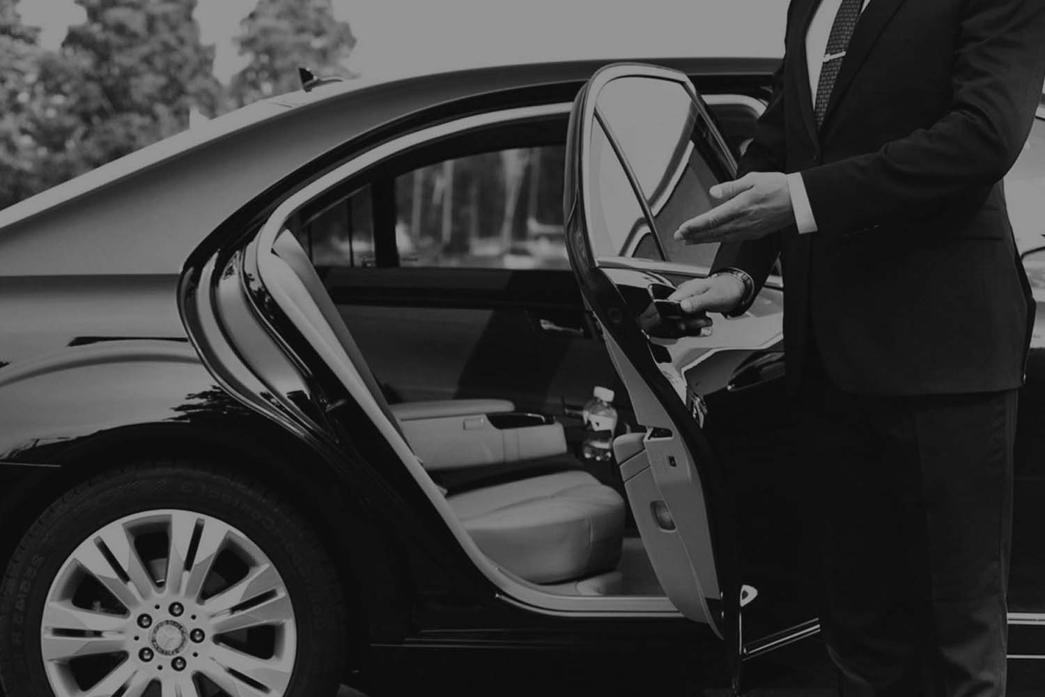 A man in suit and tie standing next to an open door of a car.