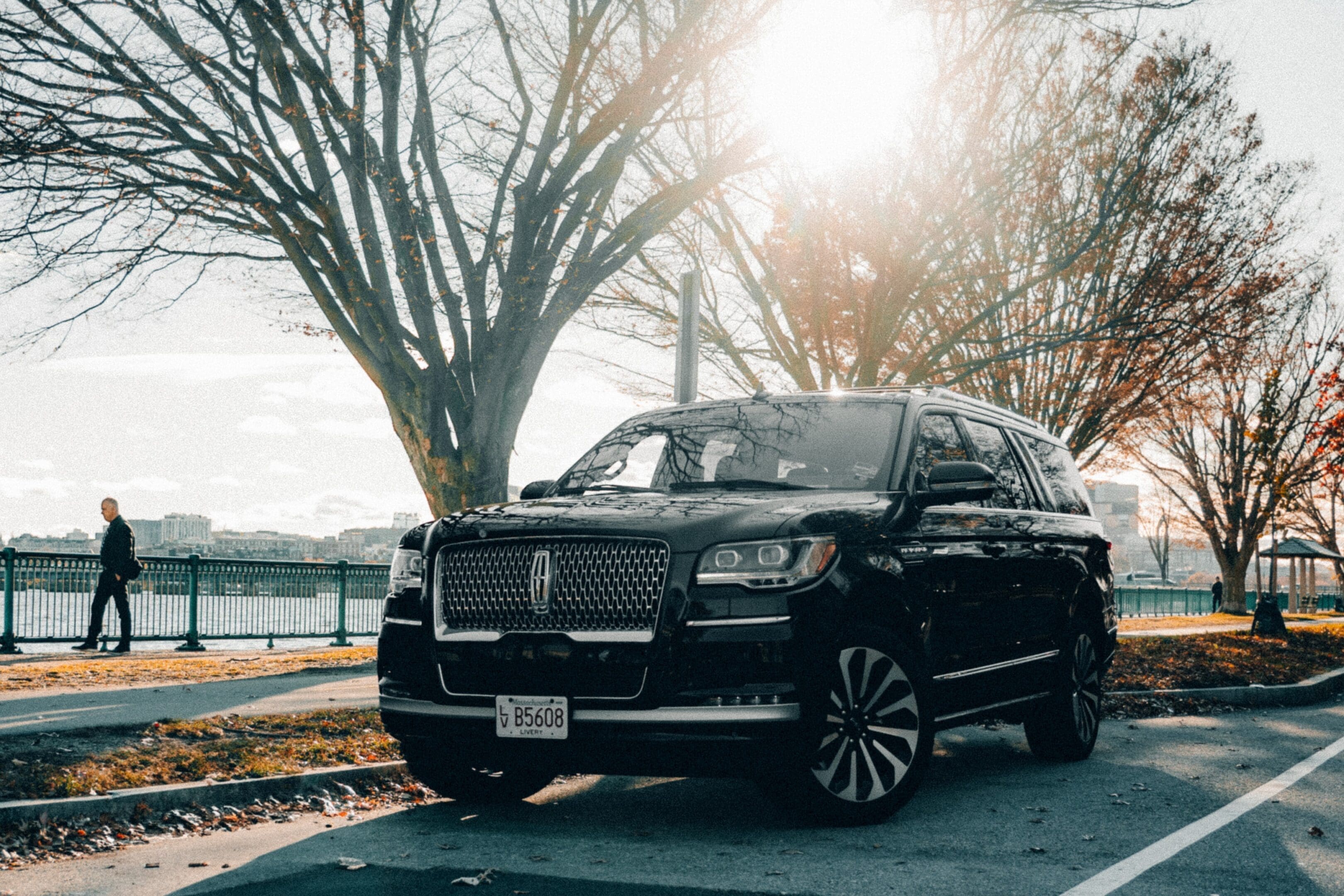 Black luxury SUV parked near trees with sunlight shining through.