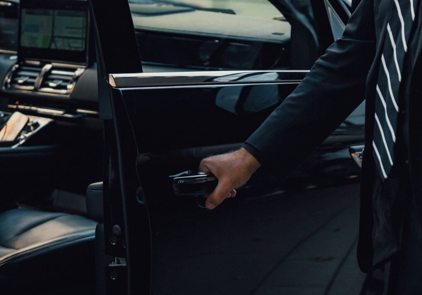 Person opening car door, dressed in formal attire with a striped tie.