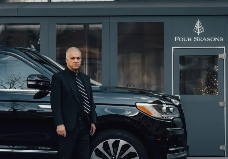 Man standing next to a black luxury SUV outside a building.
